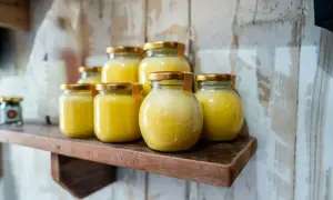 Plusieurs pots de beurre clarifié, dorés et brillants, sont alignés sur une étagère en bois rustique.