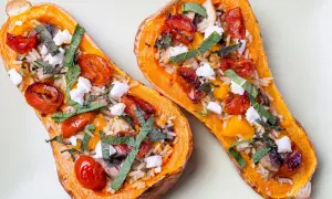 Deux moitiés de butternut au four garnies de riz, tomates cerises rôties, champignons, fromage frais et herbes.