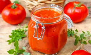 Un bocal de coulis de tomates maison, entouré de tomates fraîches et de basilic, prêt à sublimer vos plats.