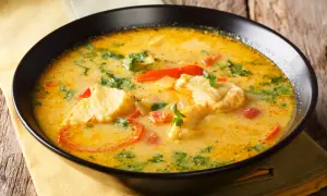 Un bol d'aigo boulido, une soupe de poisson crémeuse avec des morceaux de poisson, des tomates et des herbes fraîches, sur une serviette jaune.