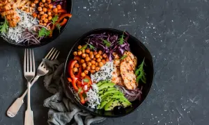 Deux bols de salade composée colorée avec poulet grillé, riz, avocat, pois chiches et chou rouge.