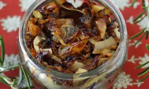 Un bocal rempli de confit d'oignon caramélisé, prêt à être dégusté. Une cuillère dorée y est plongée.