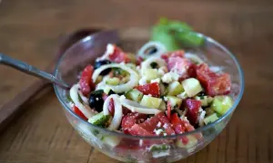 Salade cretoise fraîche et colorée dans un bol en verre, avec des tomates, concombres, oignons, olives et feta.