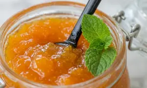 Un pot de confiture abricot maison, garni d'une feuille de menthe fraîche, prêt à être dégusté.