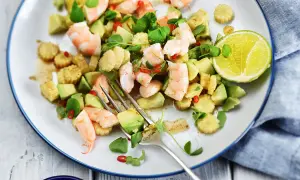 Salade avocat crevette fraîche et colorée, garnie de maïs, piment et herbes, avec une tranche de citron vert.