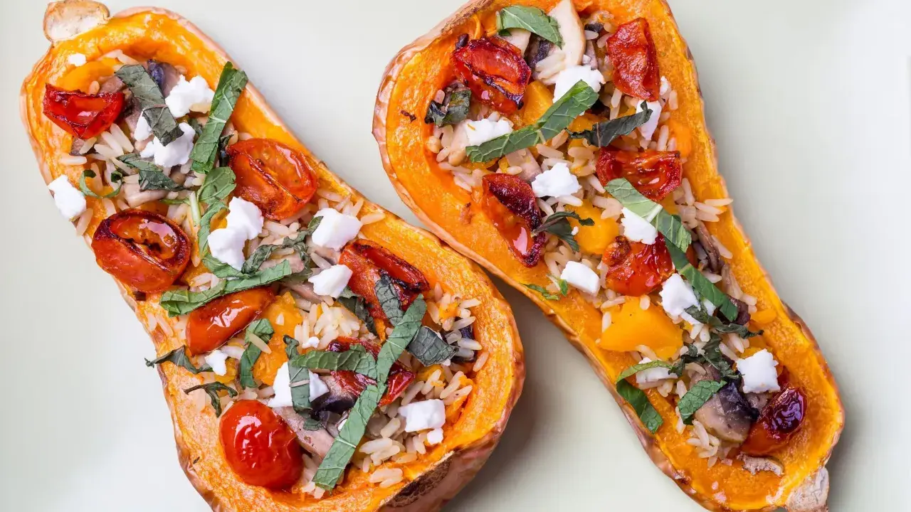 Deux moitiés de butternut au four garnies de riz, tomates cerises rôties, champignons, fromage frais et herbes.