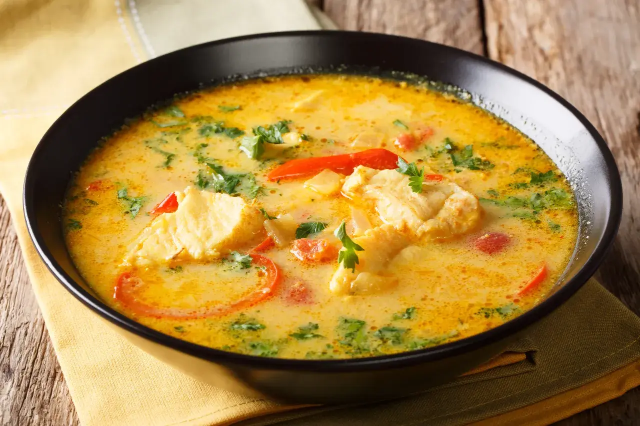 Un bol d'aigo boulido, une soupe de poisson crémeuse avec des morceaux de poisson, des tomates et des herbes fraîches, sur une serviette jaune.