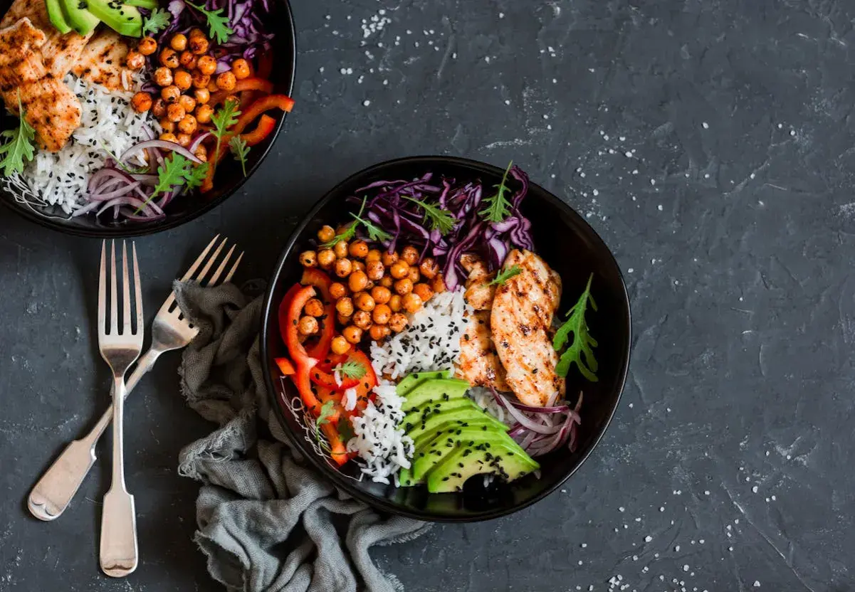 Deux bols de salade composée colorée avec poulet grillé, riz, avocat, pois chiches et chou rouge.