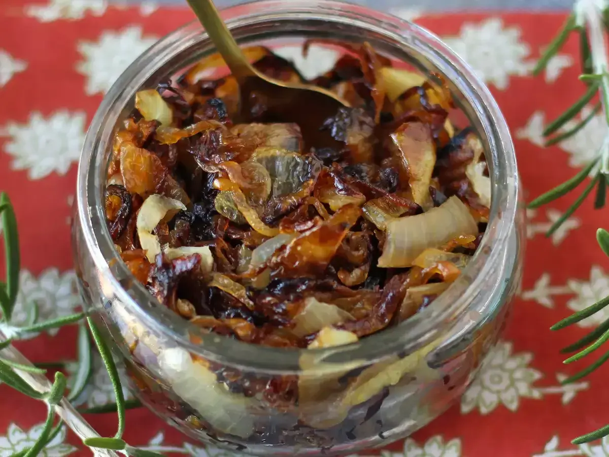 Un bocal rempli de confit d'oignon caramélisé, prêt à être dégusté. Une cuillère dorée y est plongée.