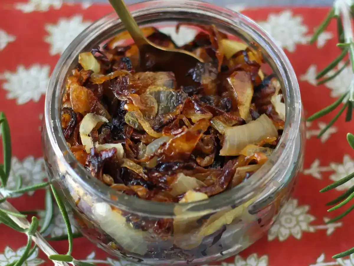 Un bocal rempli de confit d'oignon caramélisé, prêt à être dégusté. Une cuillère dorée y est plongée.