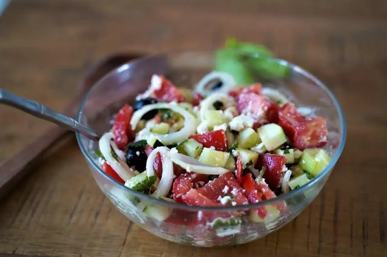 Salade cretoise fraîche et colorée dans un bol en verre, avec des tomates, concombres, oignons, olives et feta.
