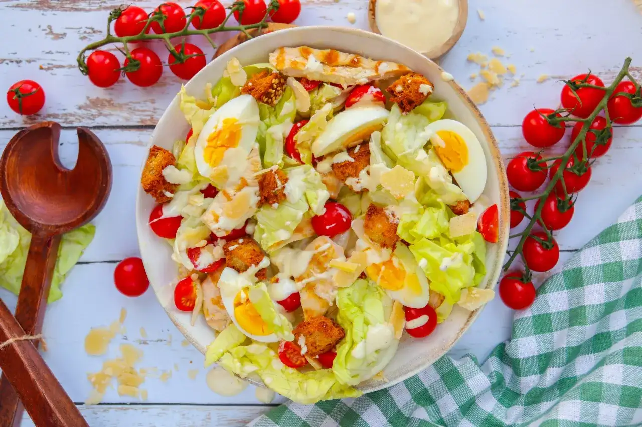 Salade César appétissante : laitue, poulet grillé, œufs durs, tomates cerises, croûtons et copeaux de parmesan. Une recette parfaite pour un repas frais.