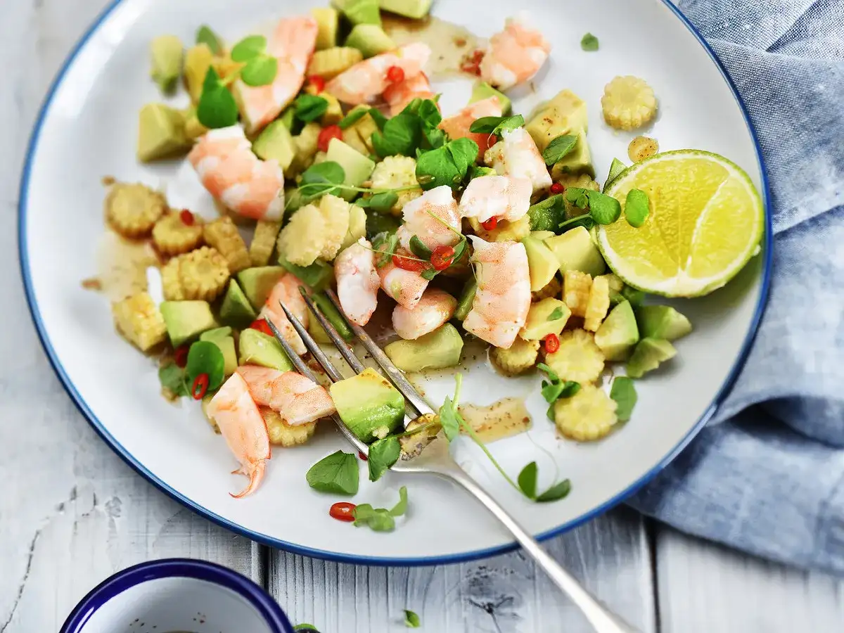 Salade avocat crevette fraîche et colorée, garnie de maïs, piment et herbes, avec une tranche de citron vert.