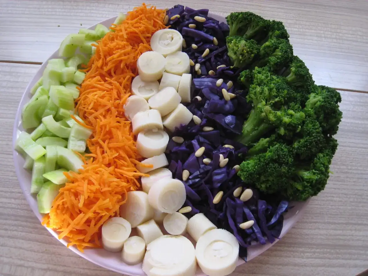 Une salade composée colorée avec des concombres, carottes râpées, cœurs de palmier, chou rouge et brocolis.
