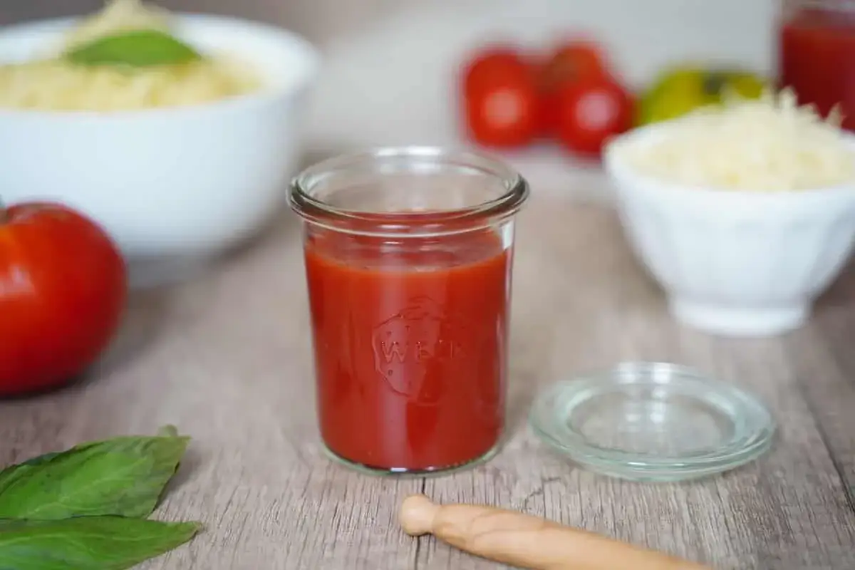 Un pot de coulis de tomates maison, prêt à être utilisé pour une recette italienne. Des tomates fraîches et du basilic à côté.