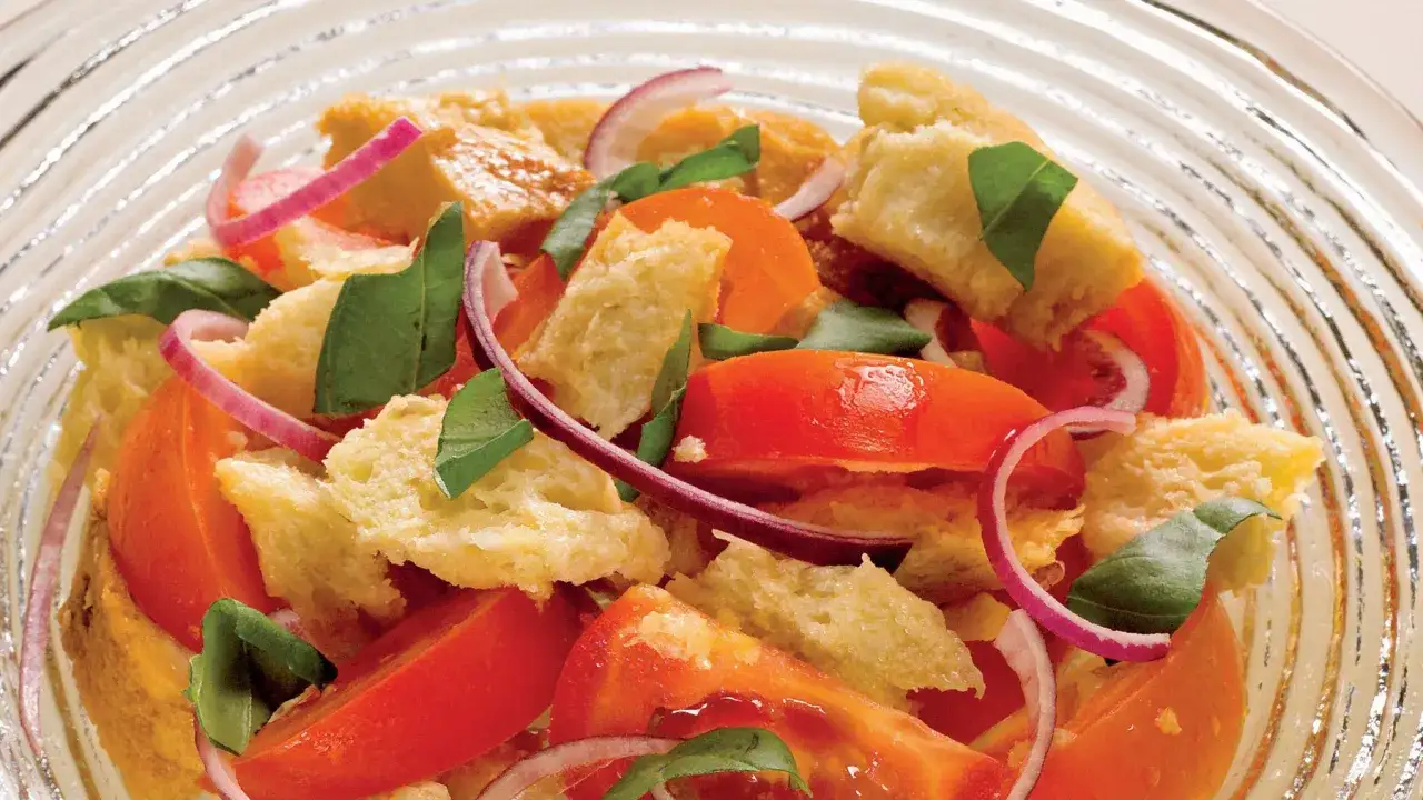 Salade estivale de panzanella recette : tomates juteuses, pain croustillant, oignons rouges et basilic frais dans un bol en verre.