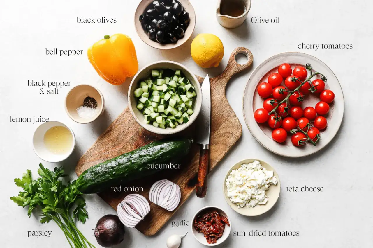 Ingrédients pour une recette salade : concombre, tomates cerises, poivron jaune, olives noires, feta, oignon rouge, persil, citron, ail, tomates séchées, huile d'olive.