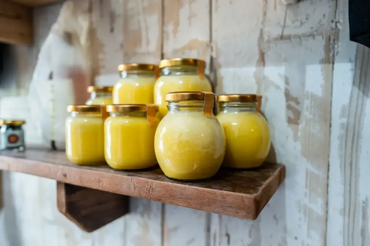Plusieurs pots de beurre clarifié, dorés et brillants, sont alignés sur une étagère en bois.