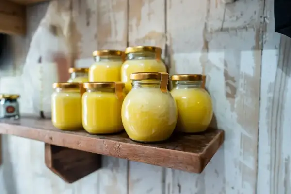 Plusieurs pots de beurre clarifié, dorés et brillants, sont alignés sur une étagère en bois rustique.