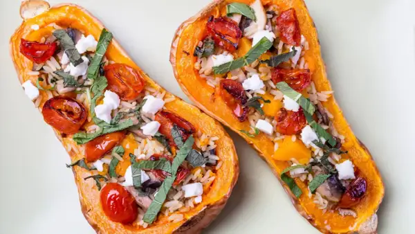 Deux moitiés de butternut au four garnies de riz, tomates cerises rôties, champignons, fromage frais et herbes.