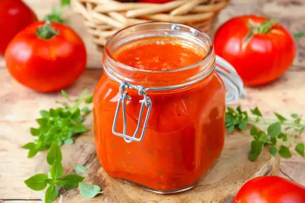 Un bocal de coulis de tomates maison, entouré de tomates fraîches et de basilic, prêt à sublimer vos plats.