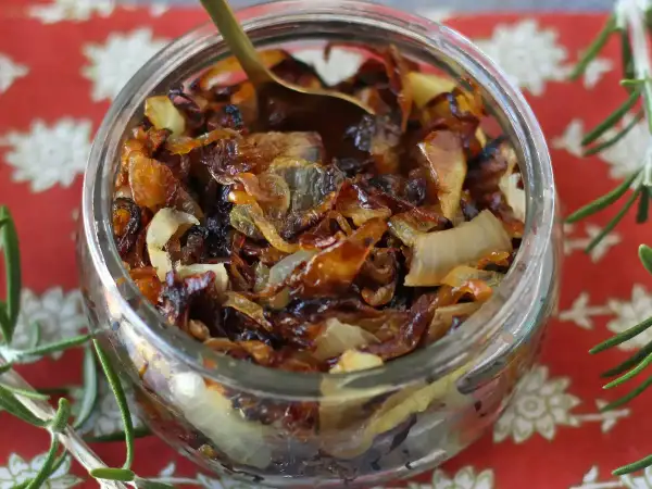 Un bocal rempli de confit d'oignon caramélisé, prêt à être dégusté. Une cuillère dorée y est plongée.